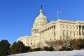 The U.S. Capitol building, on front of a blue sky. In the foreground, snow is on the ground. 