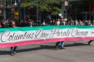 People walking in a parade with a Columbus Day banner.