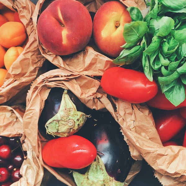 Overhead photo of fruit in paper bags, including stone fruit, cherries, eggplant, tomatoes, and spinach