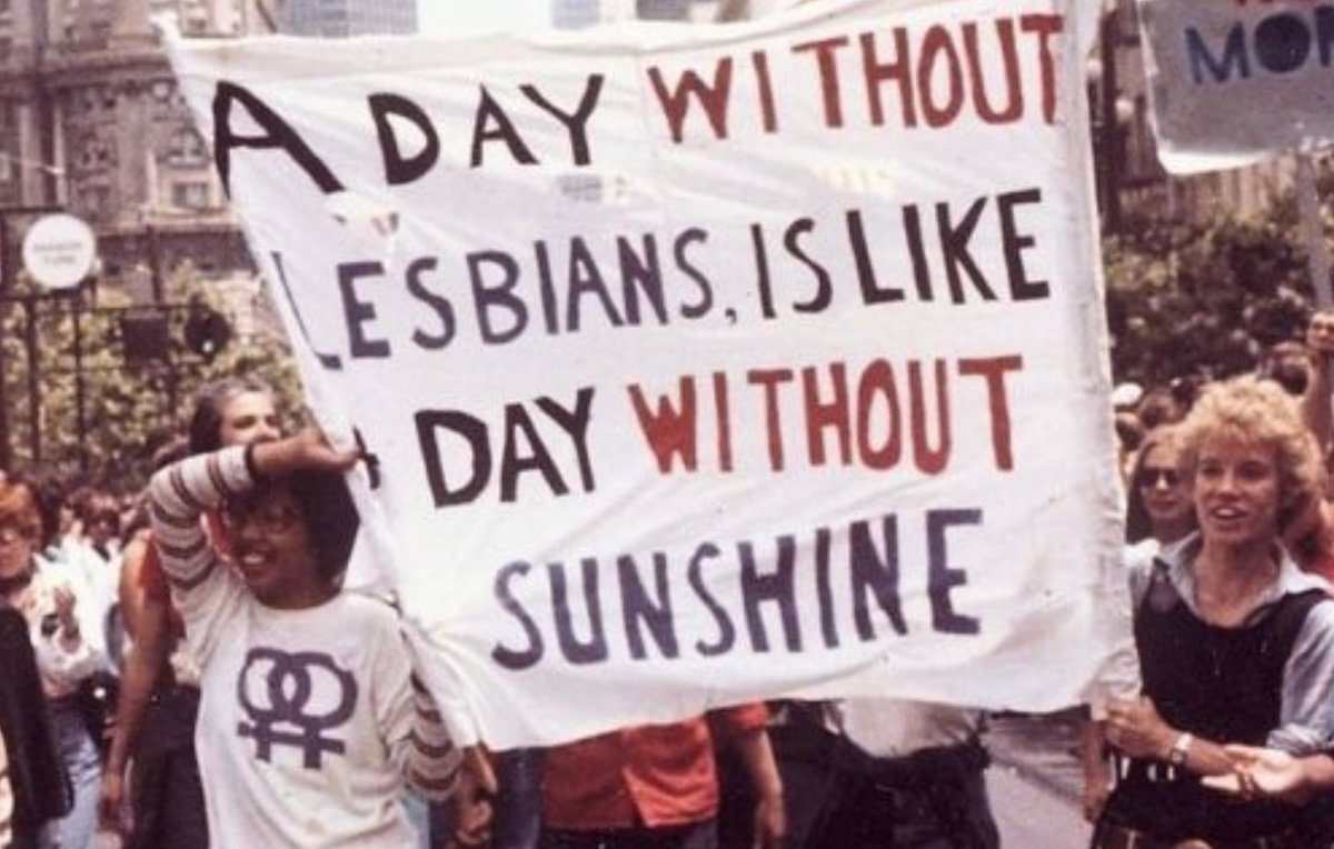 A photo of people marching and holding up a banner that says "A day without lesbians is like a day without sunshine." It's from the gay freedom day parade in San Francisco in June 1979.