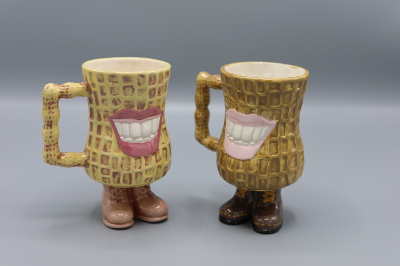 Two mugs, both shaped like peanuts with two feet wearing boots each.  Both mugs have a big smile reminiscent of President Carter's smile.  They are angled slightly towards each other.