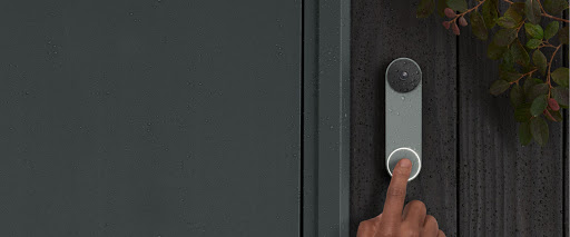 Nest Doorbell is on the front of a house. Rain droplets are on it and a finger is in frame as it rings the bell. 