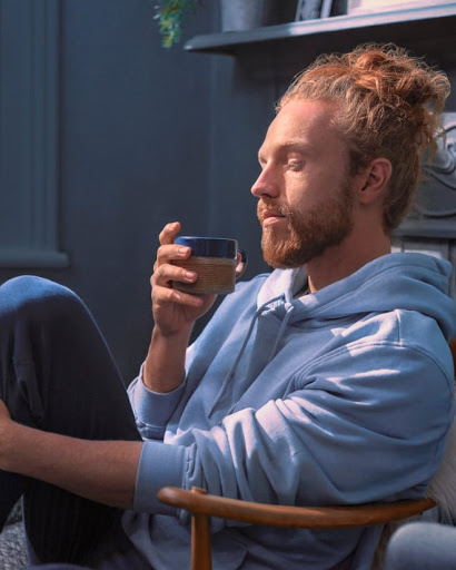 Man winds down in his bedroom with lights dimmed as he sips a cup of evening tea.