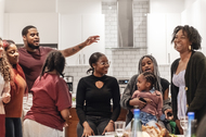 A big family of many generations laughing and singing together in a kitchen.