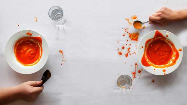 Two bowls of soup, each being eaten with a regular spoon vs a sup spoon. The one with the regular spoon has spills all around.