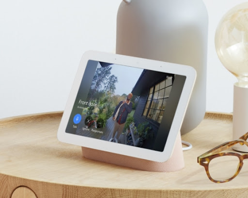 Nest Hub (2nd gen) is on a wooden table inside a home. On the display, a delivery person is at the front door holding a package.