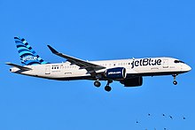 A white plane with the word "jetBlue" painted in the front and a blue tailfin on the back prepares to land as its landing gear is deployed