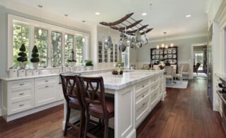 A bright kitchen with white marble countertops and wooden chairs.