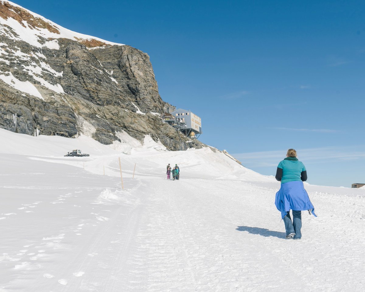 The same person as last picture walking the last bit of path towards a mountain peak. There's a metallic box-like building built aginst it.