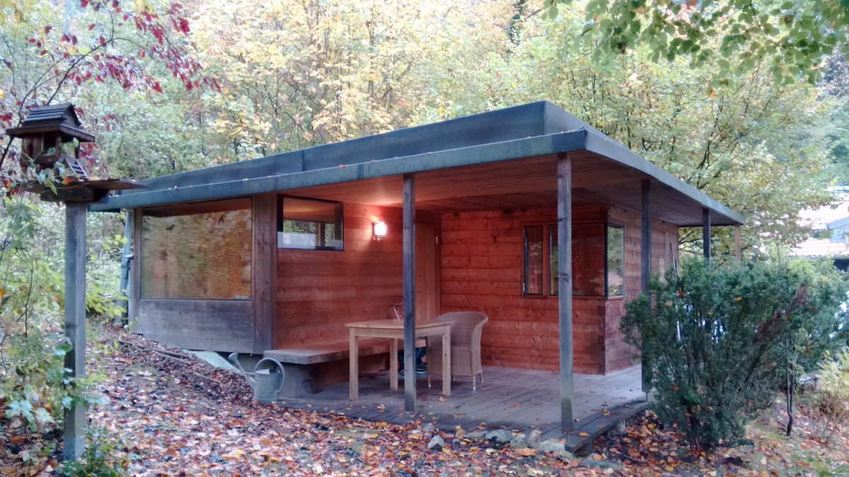 Our cosy little cabin. It looks modern and angular. You're looking at a nearly square floor with one corner cut out to create a terrace, covered by the same roof. The building is wooden but with clean modern windows.