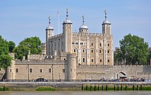 A keep seen from a river, rising behind a gate. The keep is large, square in plan, and has four corner towers, three square and one round, all topped by lead cupolas.