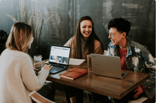 3 mulheres sorrindo na mesa com computadores