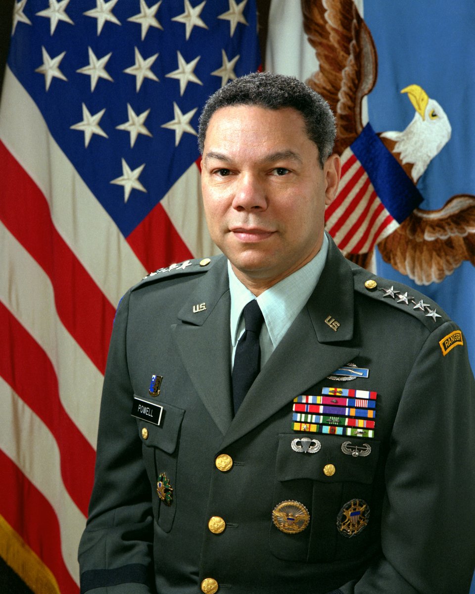 Portrait of a man in military uniform, heavily decorated, seated in front of a flag