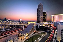 A train station built over a busy intersection in front of several skyscrapers at sunset.