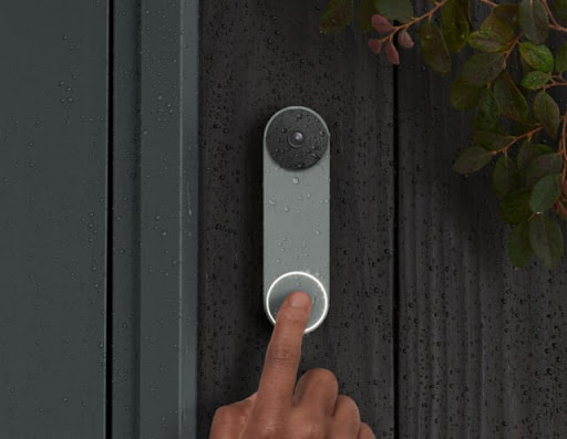Nest Doorbell is on the front of a house. Rain droplets are on it and a finger is in frame as it rings the bell. 