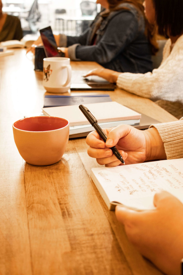 A hand holding a pen and writing in a notebook held by another hand