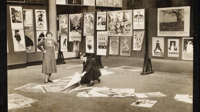 A woman and a man installing a poster exhibition at the V&A, Emil Otto Hoppé, 1931. E.655-1996