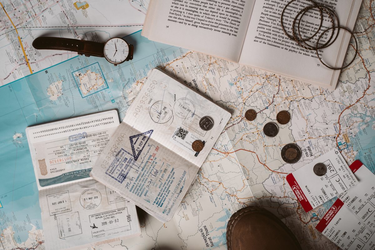 Passport and travel documents, a watch, an open book, and coins on top of paper maps