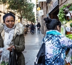 Two young women buy vegetables outside a shop.