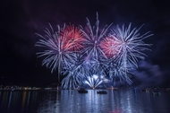 blue and red fireworks in the sky at night, over a lake