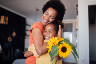 African American mother hugging her daughter and holding sunflowers.