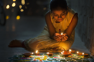 A little indian girl sitting on the floor and lighting up dipa oil lamps for the Diwali celebration.