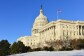 The U.S. Capitol building, on front of a blue sky. In the foreground, snow is on the ground. 