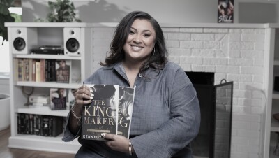 A woman sits in a living room setting, holding two books she wrote and self-published. 