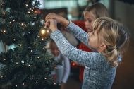 Two little girls decorating the Christmas tree with ornaments and Christmas lights.