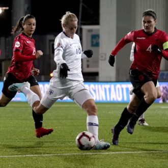 A Finnish player kicks the ball as Albanian player run behind her.