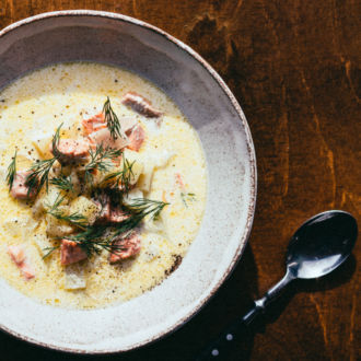 A bowl of soup, a cup and a spoon on a wooden table, viewed from above.