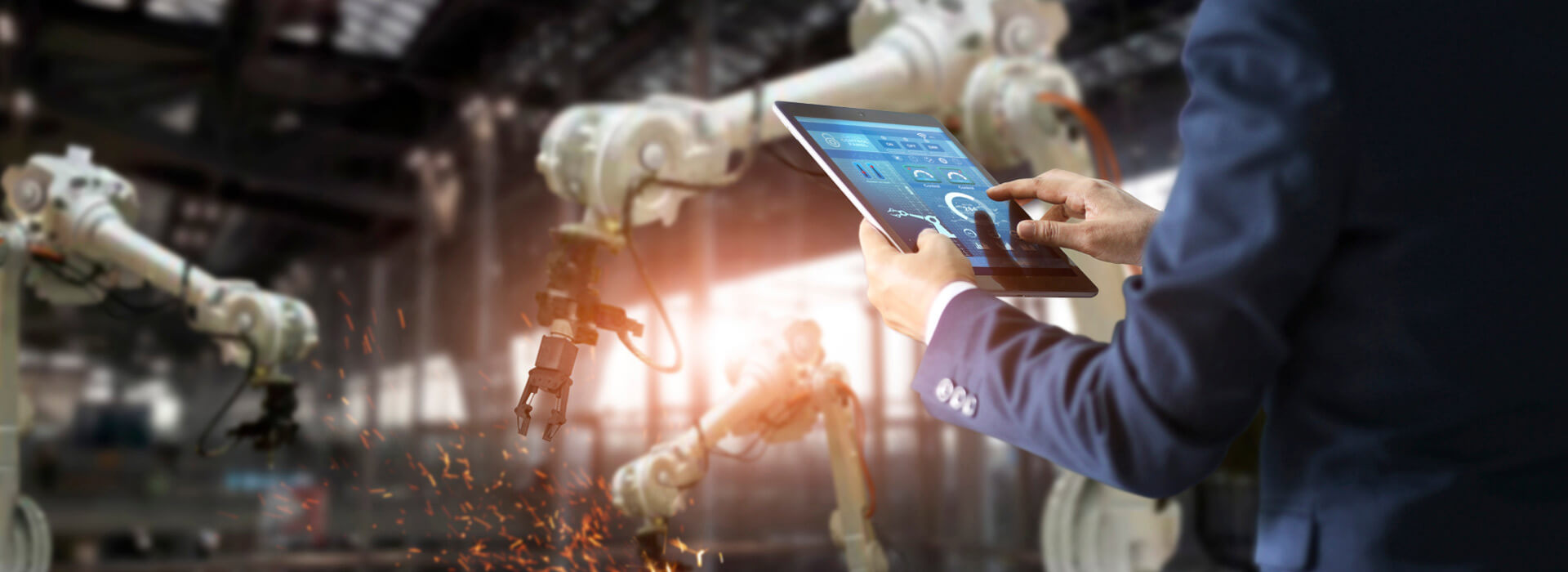 Person in a factory using a tablet to check the performance data of a robotic manufacturing arm.