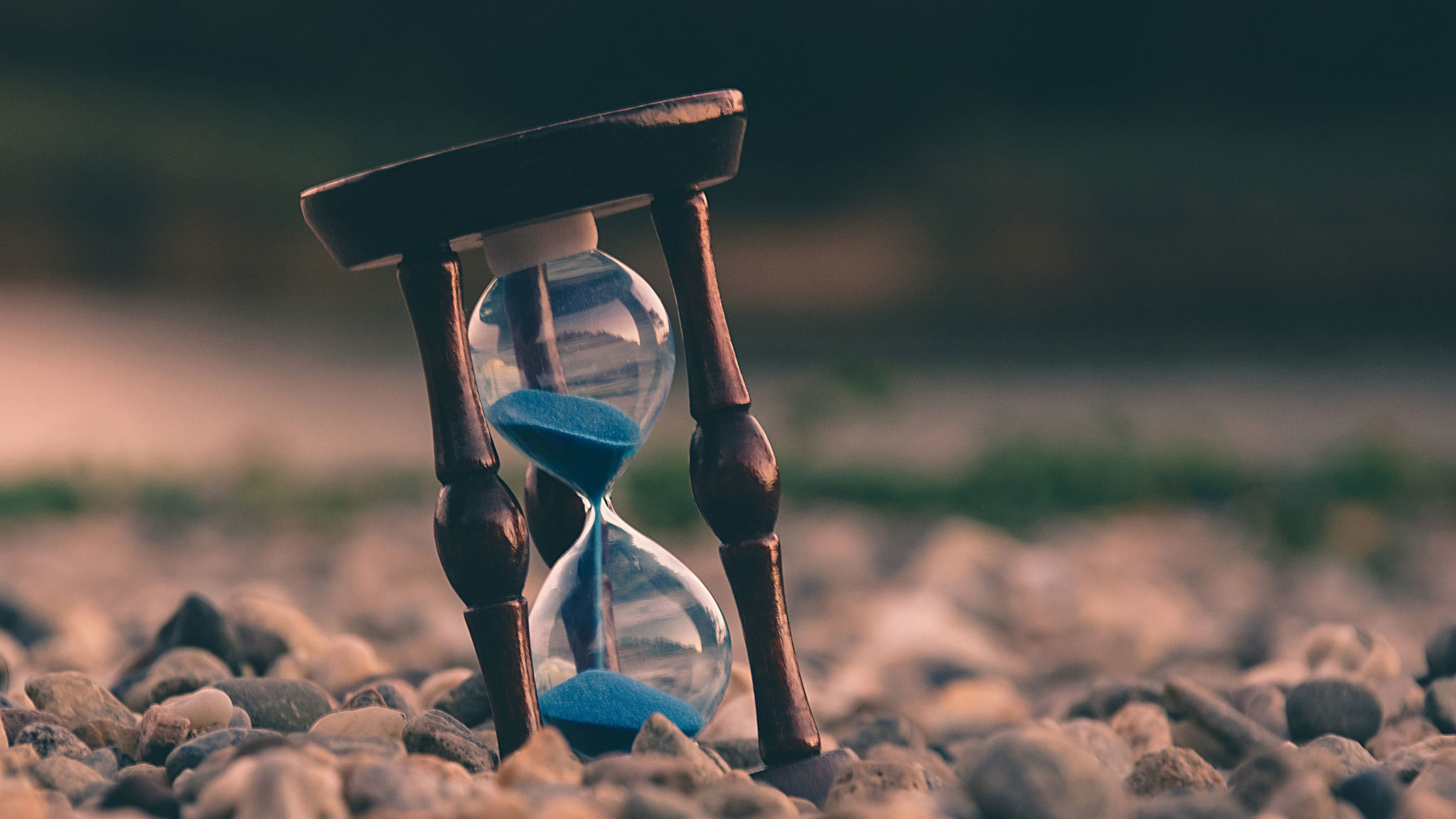 Hourglass with blue sand on a rocky surface.