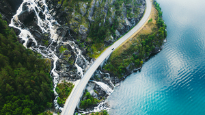 En bil kjører på en vei mellom brevann og en stor foss nedover fjellsiden.