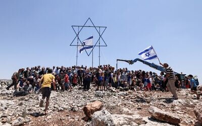 Settlers gather for a group photograph under a giant Star of David and a national flag before evacuating the newly-established wildcat outpost of Evyatar near the northern Palestinian city of Nablus in the West Bank, on July 2, 2021 (Emmanuel DUNAND / AFP)