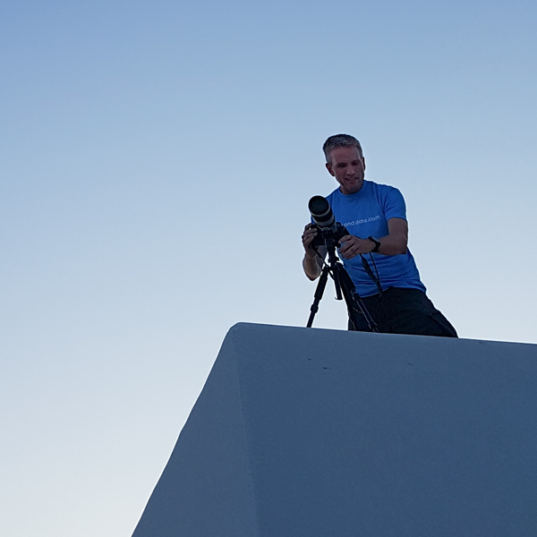 Mann steht auf dem Flachdach eines weißen Gebäudes mit einer Kamera.