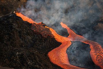 During 2 Oct, the activity continued without significant changes. At the cone, the flank vents remained active with lava spattering or low fountaining to feed lava flows, while pulsating lava fountaining became again stronger at the summit vents.
The effusive vent north from the cone remained active with quiet lava effusion as well. Favorable wind conditions and a special permit from Guardia Civil provided us with unique observation opportunities from close range. (Photo: Tom Pfeiffer)