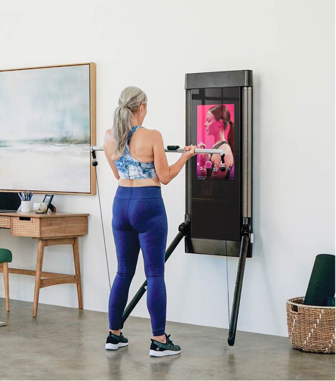 A woman performs biceps curls using her Tonal smart home gym machine.