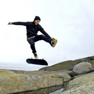 A man does a skateboard trick outside on a large rock surface.