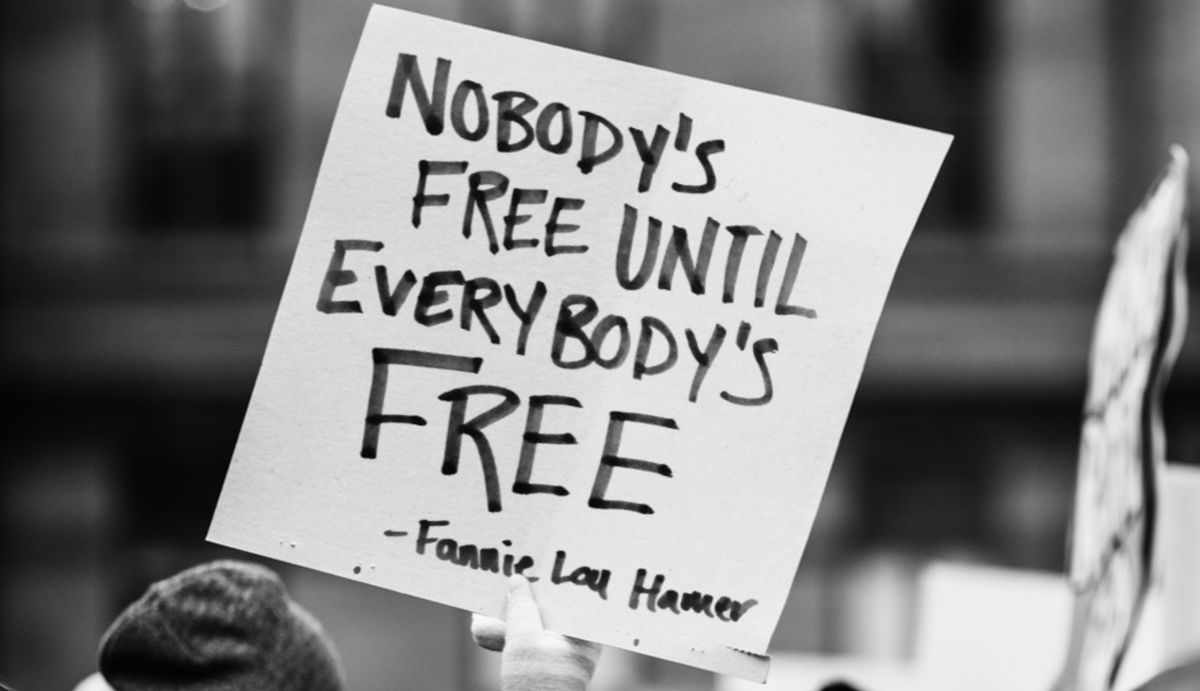 A black and white photo shows a protest sign with the famous quote from civil rights activist Fannie Lou Hamer: Nobody's free until everybody's free.