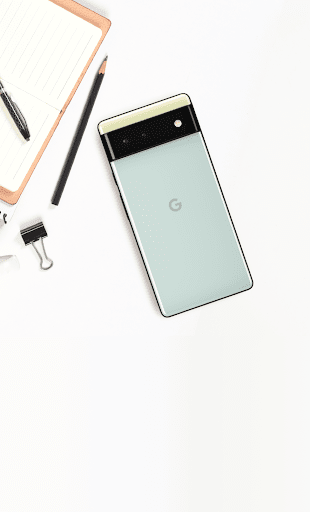 An overhead image of a Google Phone on a desktop next to a pencil, notepad, and binder clip.
