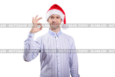 An adult confident man looks into the camera, the gesture is okay, everything is fine, dressed in everyday clothes, a light plaid shirt, a New Year's cap. Isolated, homogeneous background