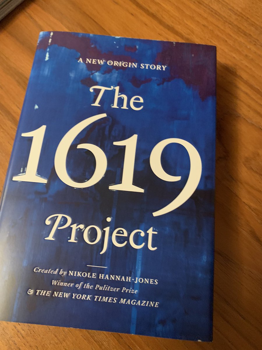 The 1619 Project book on my desk.  Other text says A New Origin Story. Created by Nikole Hannah-Jones Winner of the Pulitzer Prize and the New York Times. Gold lettering blue background.