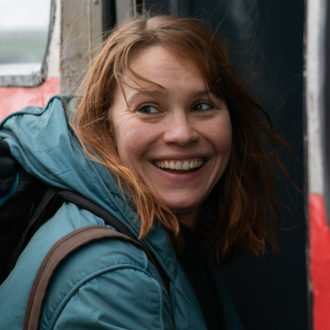 Une jeune femme portant un anorak et un sac à dos sourit.