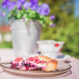 Une table est dressée en plein air avec deux tasses de café et deux assiettes remplies chacune d’une part de tarte aux baies.