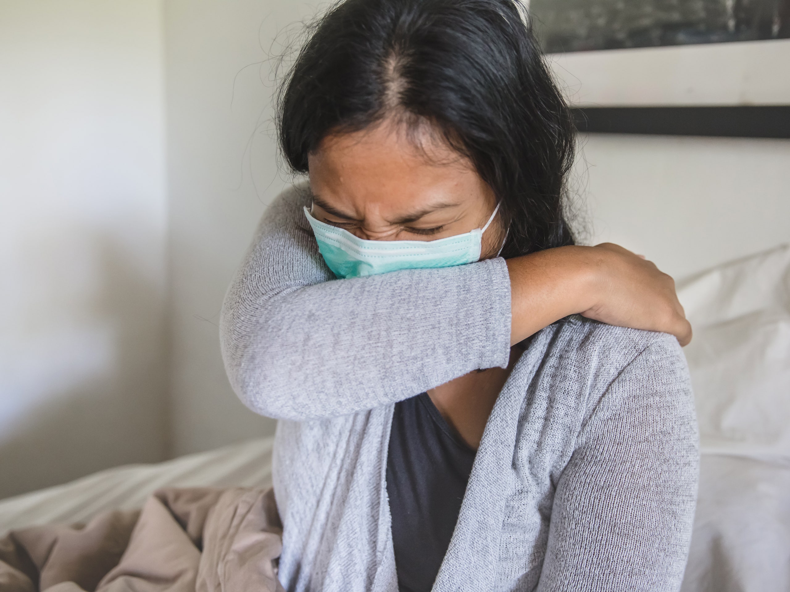 Portrait shot of Asian woman sick in bed  covering cough with elbow during home quarantine Covid 19