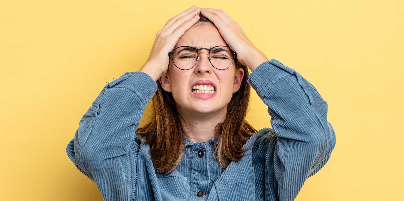 A woman grabs her head and tensely contorts her face