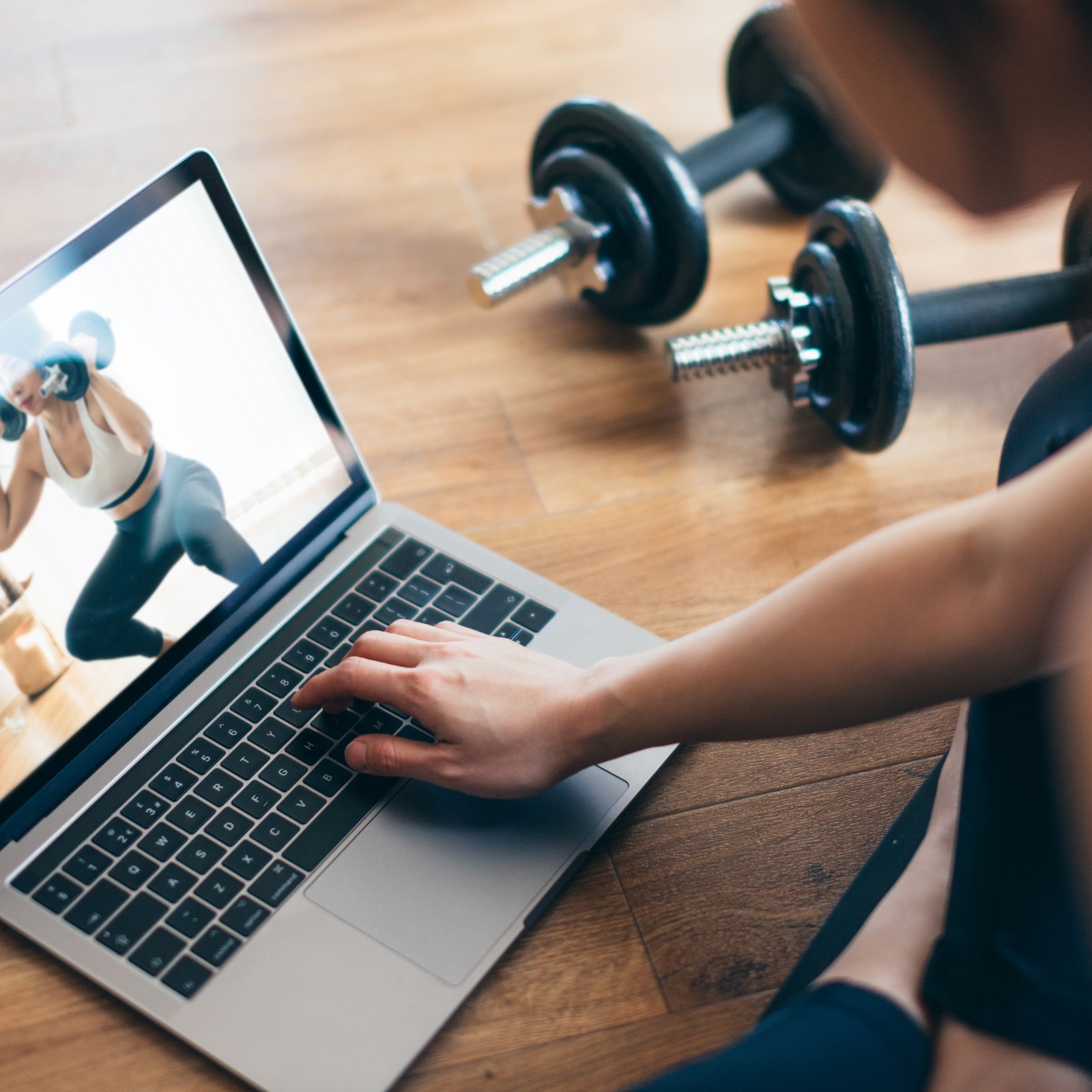 High angle view of young Asian woman practising weight training workout at home with a video lesson on laptop during the...