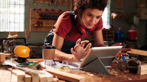 A woman in a wood working space works on a tablet. 