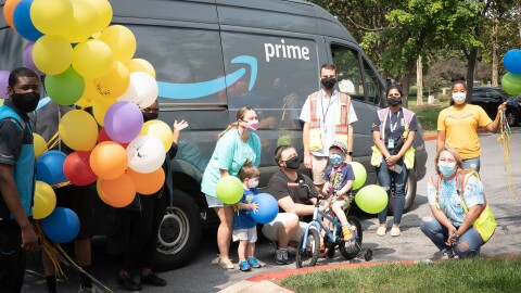 An image of a family smiling for a photo in front of an Amazon van. There are balloons and Amazon employees in the photo as well. 